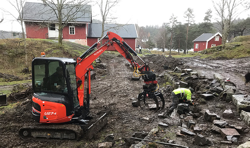 Restaurering av gamle steinmurer er et møysommelig arbeid. Eystein Greibrokk gjør handarbeidet, mens Anders Oppegaard styrer gravemaskinen. Foto: Asbjørn Aanonsen